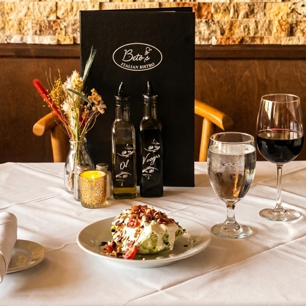A Beto's Italian Bistro table set with a wedge salad, red wine, water, and menu.