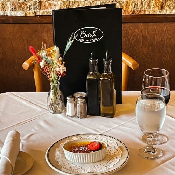 A Beto's Italian Bistro table set with creme brulee, wine, water, and menu.
