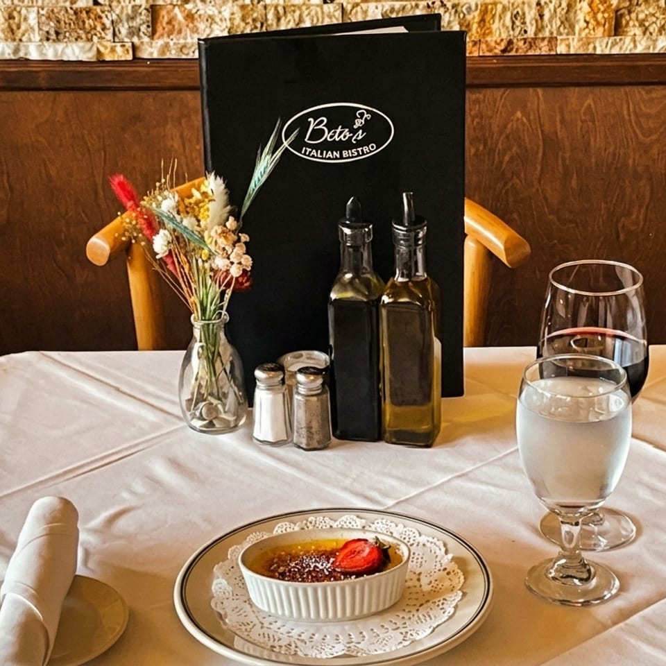 A Beto's Italian Bistro table set with creme brulee, wine, water, and menu.