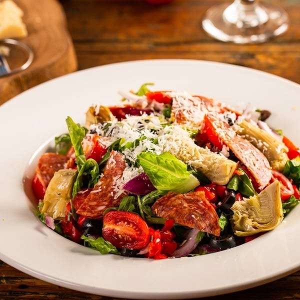 A vibrant Italian salad with salami, artichokes, tomatoes, and grated cheese on a rustic wooden table.