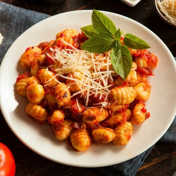 Plate of gnocchi with tomato sauce, parmesan, and basil, next to bread and a tomato.